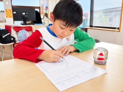 A child drawing at a desk beside a snow globe.