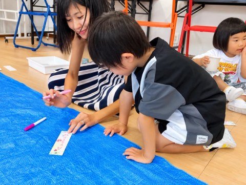 A child drawing on paper strips with help from an adult.