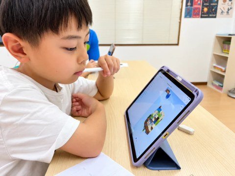 A child studying a tablet screen at a classroom desk.