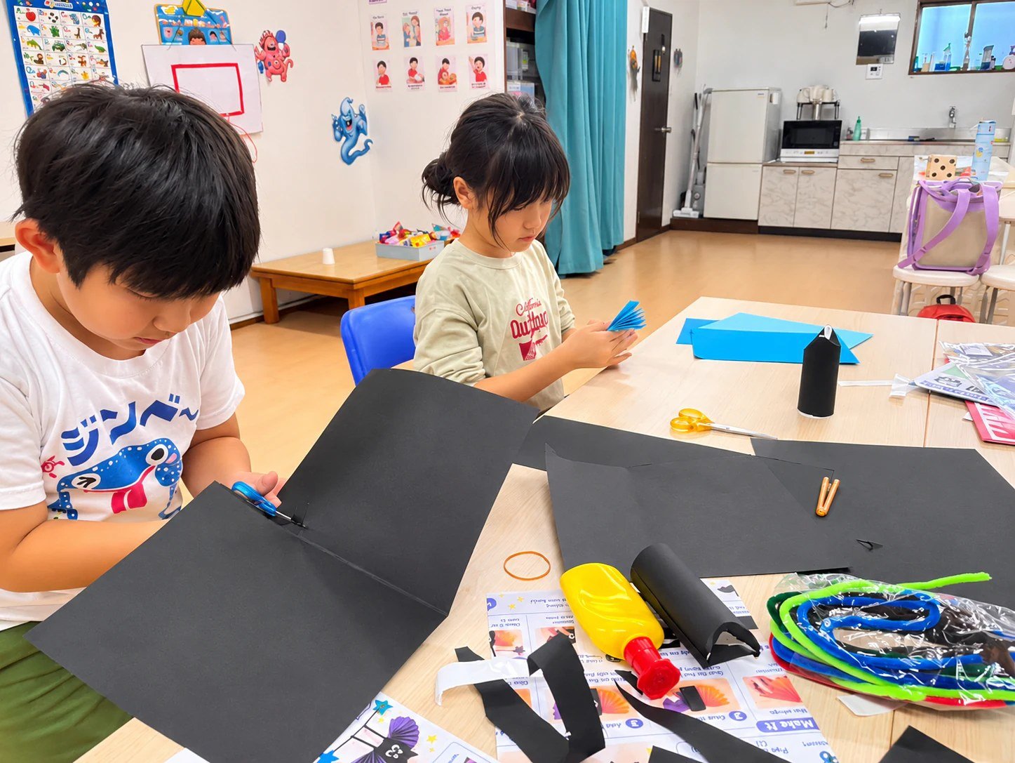 Children cutting paper with scissors and folding blue paper.