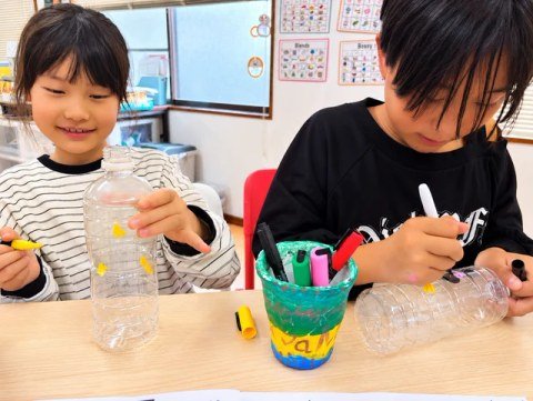 Children decorating clear plastic bottles with markers and stickers.
