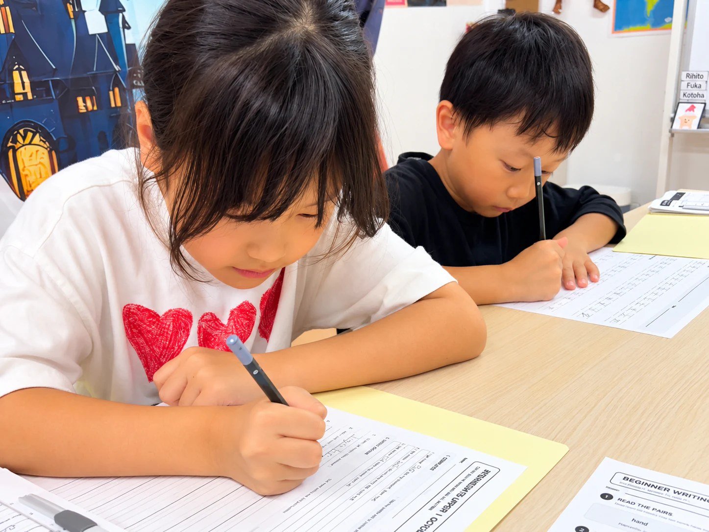 Children writing on English worksheets with pencils in class.