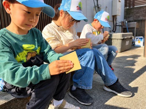 Children wearing caps and working with sandpaper outdoors.