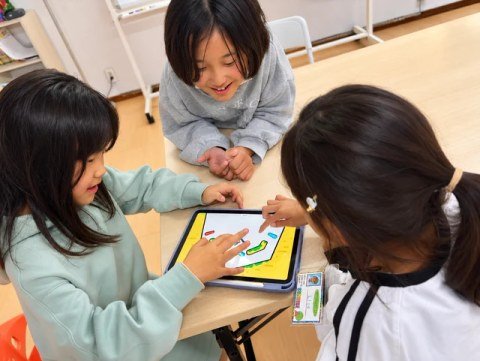 Children working together on a shape puzzle on a tablet.