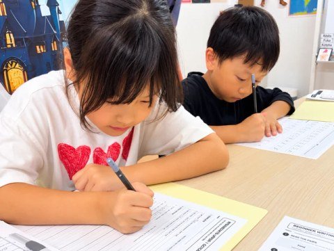 Children using pencils to complete English worksheets.