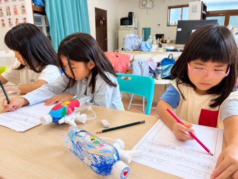 Children working on worksheets with decorated bottles on their desks.
