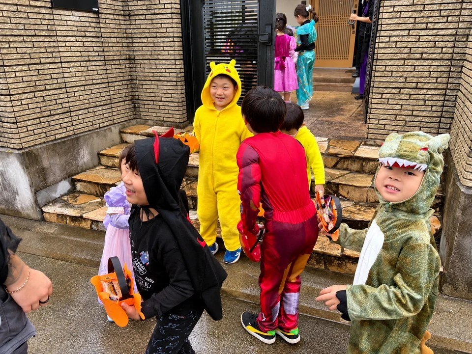 Children in costumes holding orange baskets outside a building entrance.