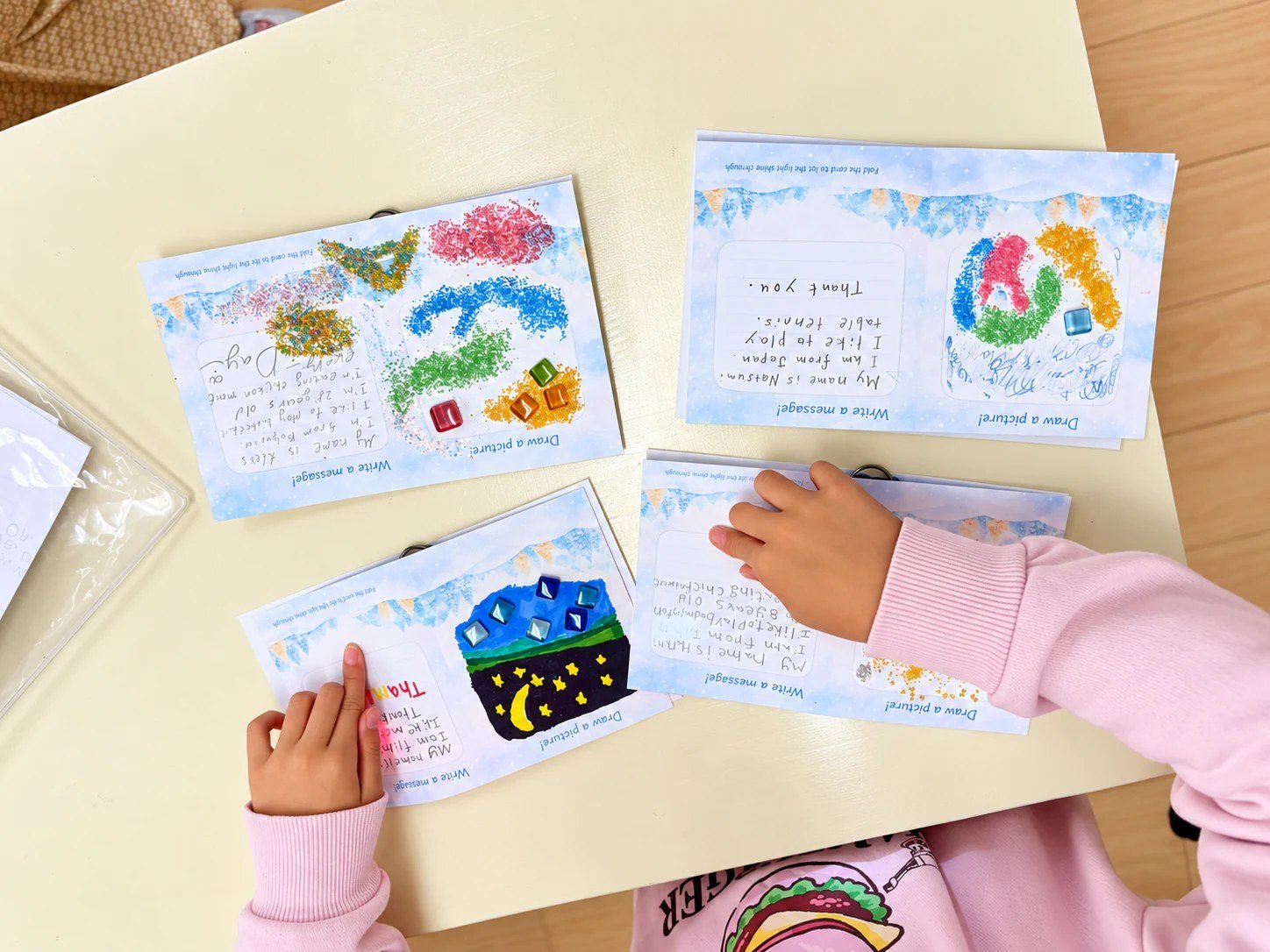 Handmade cards with illustrations and English messages beside a child’s hands.